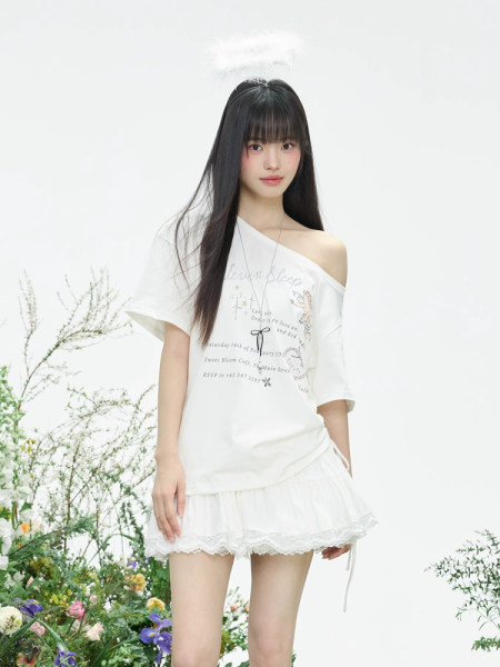 Model wearing a white off-shoulder oversized graphic top with a white lace-trim mini skirt