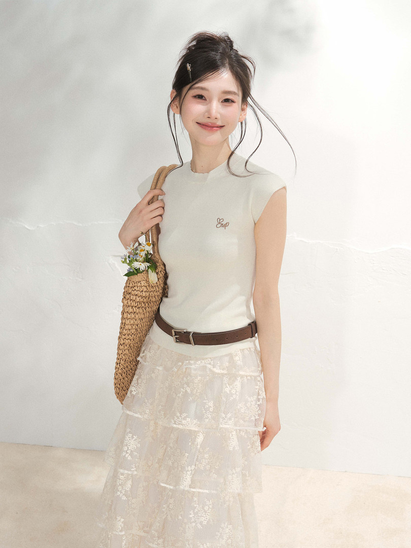 Woman wearing a cream sleeveless top with a lace skirt and woven bag