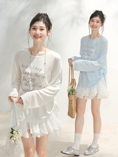 Two women modeling loose long-sleeve printed tops with white layered skirts in a bright studio
