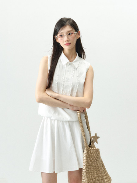 Model wearing a white sleeveless blouse and matching skirt with a woven tote bag