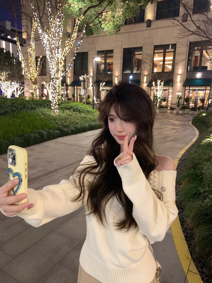 Woman wearing a cream off-shoulder knit sweater in an outdoor nighttime selfie