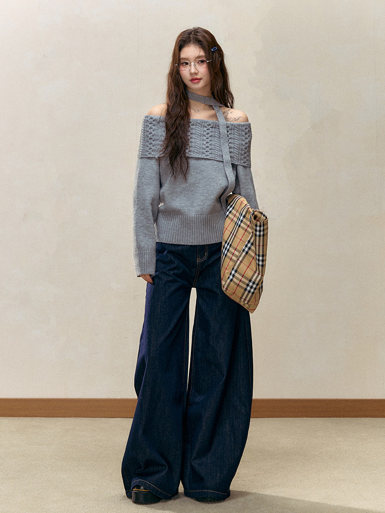 Woman wearing a gray off-shoulder knit sweater with wide-leg dark jeans and a plaid shoulder bag