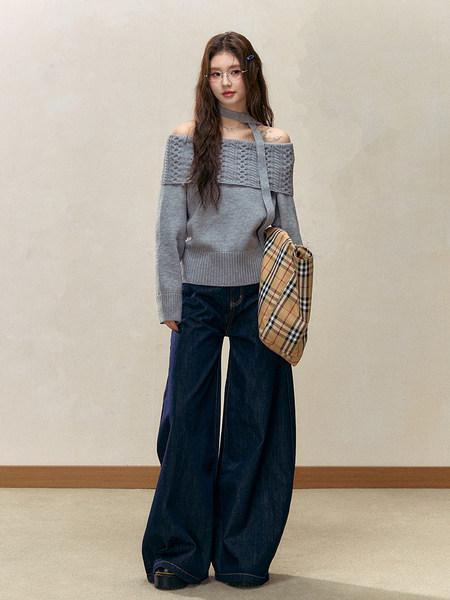 Woman wearing a gray off-shoulder knit sweater with wide-leg dark jeans and a plaid shoulder bag