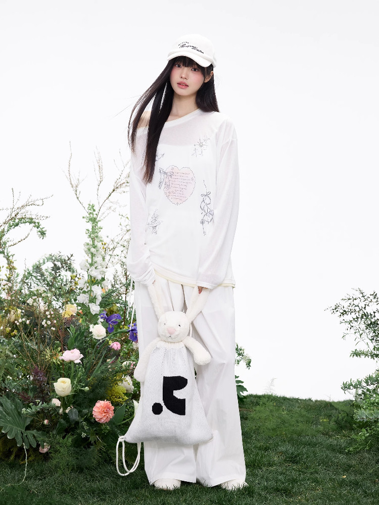 Model wearing a white long-sleeve top and wide-leg pants with a white cap, holding a bunny bag