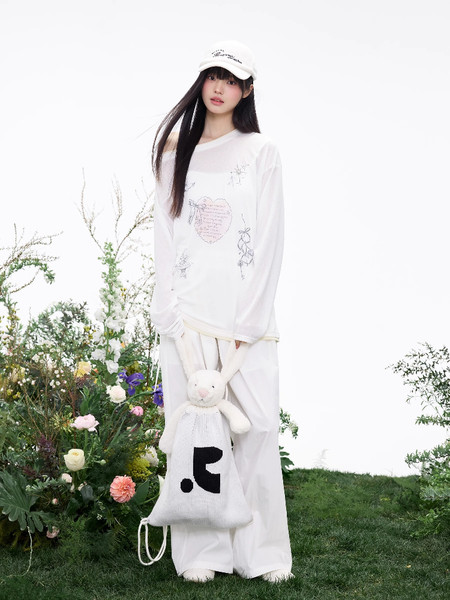 Model wearing a white long-sleeve top and wide-leg pants with a white cap, holding a bunny bag