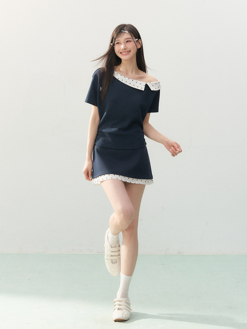 Model wearing a navy off-shoulder top and matching skirt with white polka dot trim