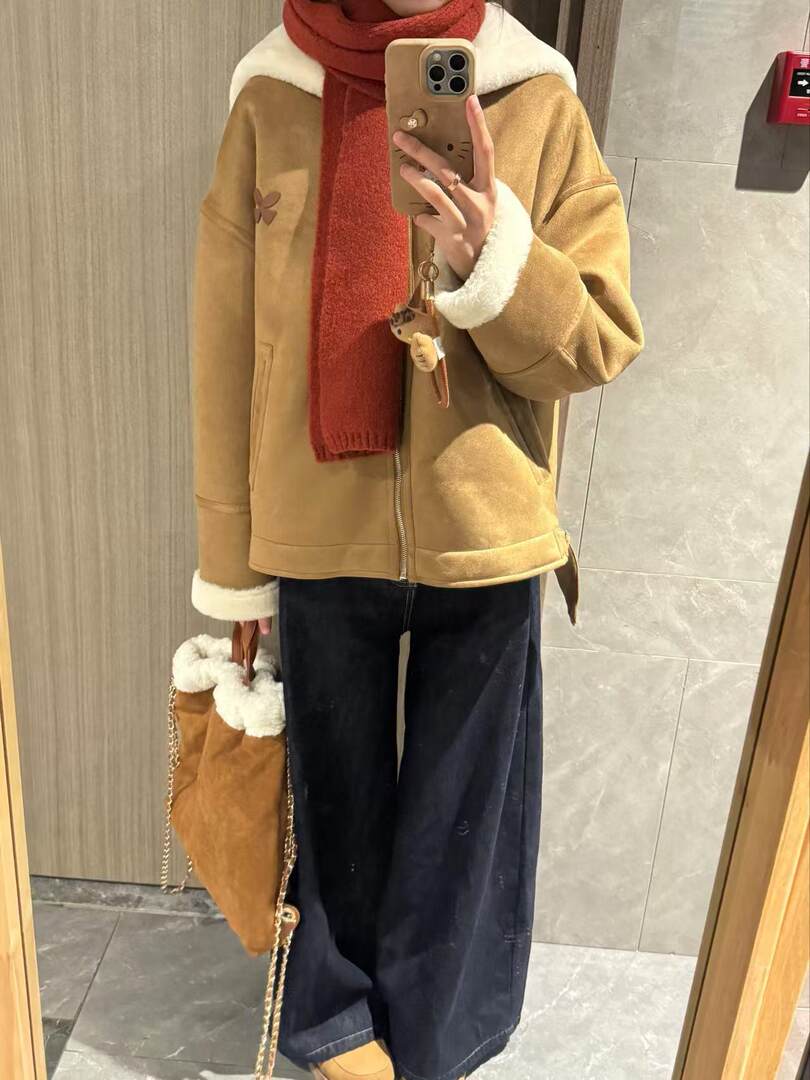 Mirror selfie of a person wearing a tan shearling-lined coat with a red scarf and carrying a brown bag