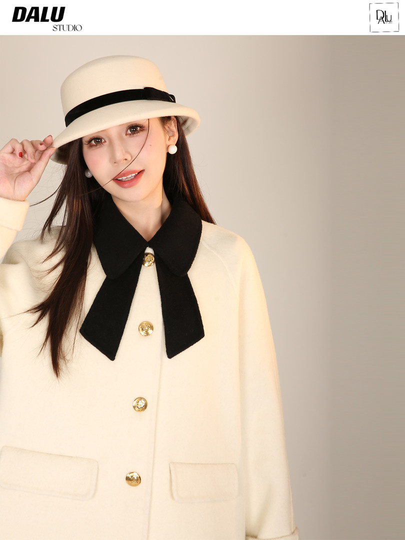 Model wearing a cream coat with black bow detail and matching hat