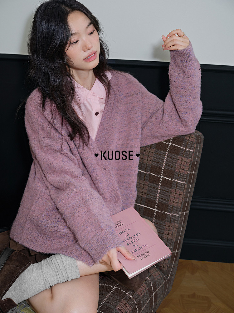 Woman wearing a purple knit cardigan over a pink top while seated on a chair