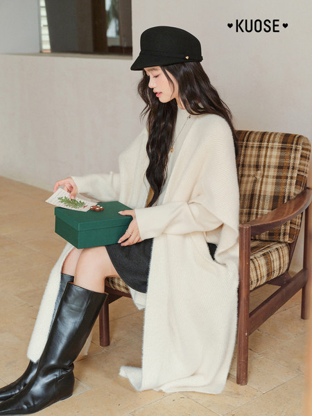 Model wearing a cream oversized knit coat with black boots and a black hat
