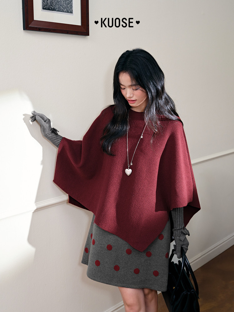 Model wearing a burgundy knit poncho with a gray polka dot skirt and gloves