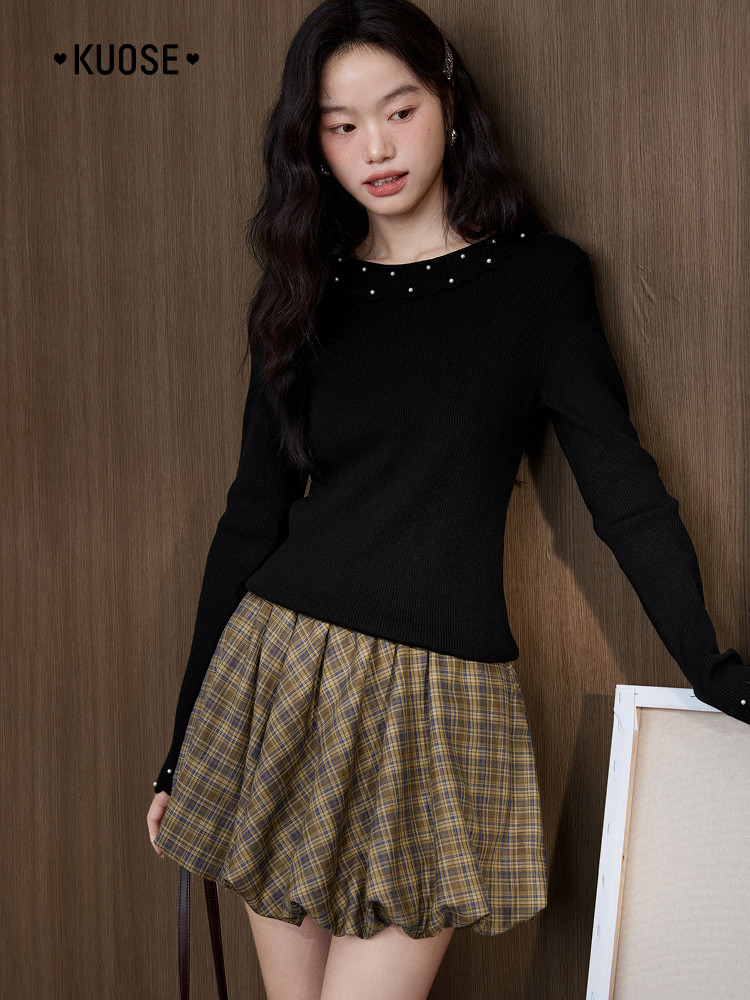 Model wearing a black long-sleeve top with pearl details and a plaid bubble skirt
