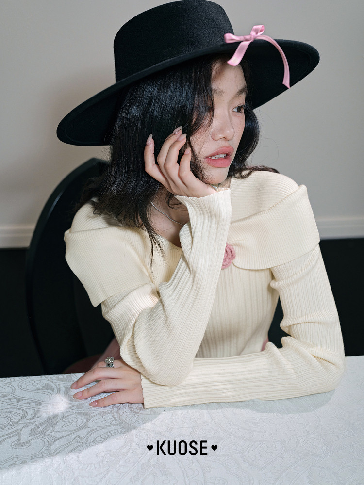 Model wearing a cream off-shoulder ribbed top with a black wide-brim hat