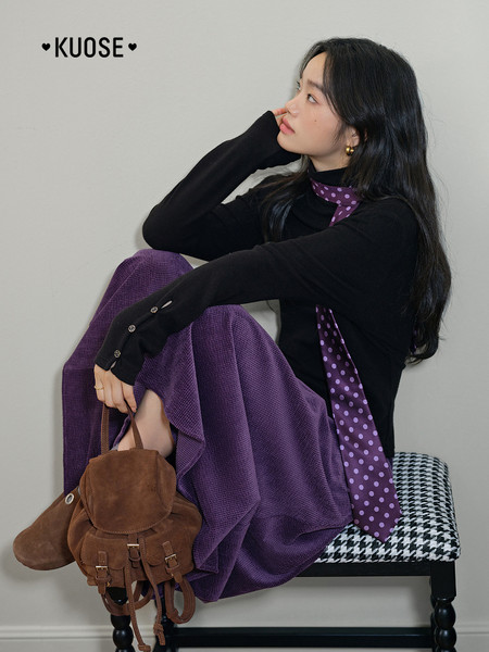 Fashion model wearing a black turtleneck, purple skirt, and scarf with a brown backpack