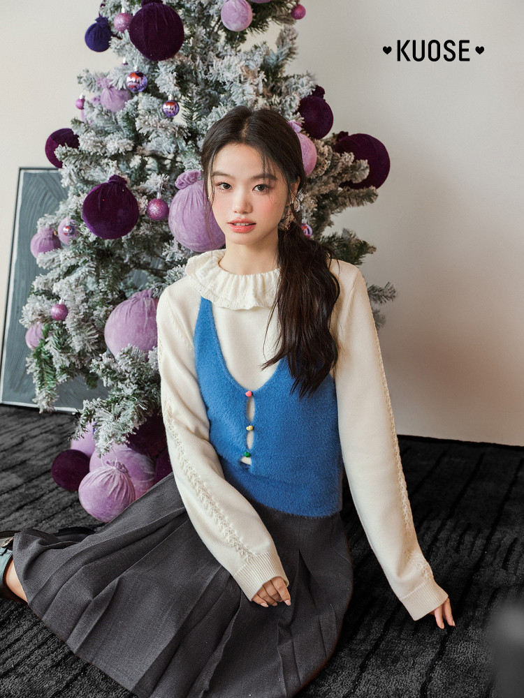 Woman wearing a cream blouse with a blue knit vest and gray pleated skirt in a festive setting