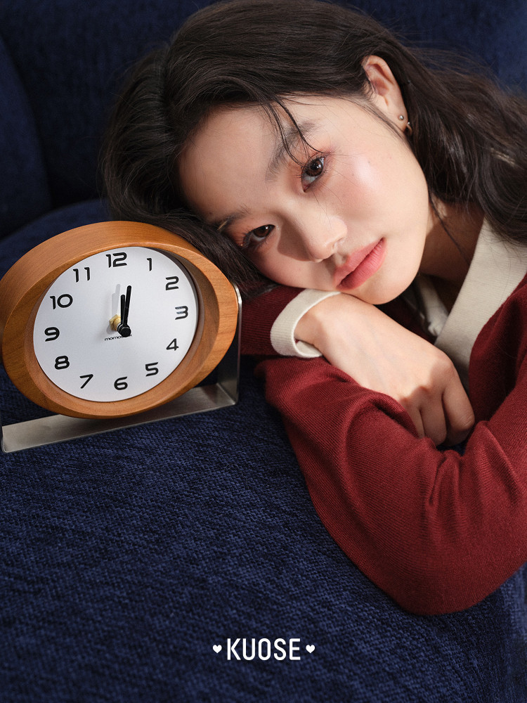 Model wearing a red knit cardigan beside a wooden table clock