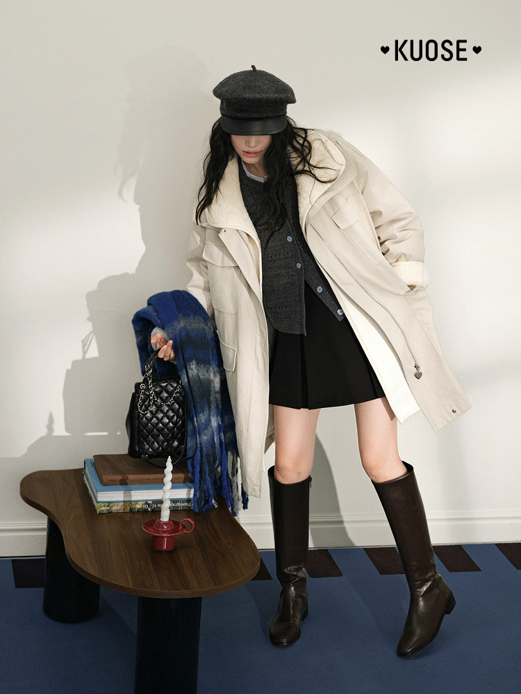 Fashion model wearing a cream oversized coat with black skirt and knee-high boots