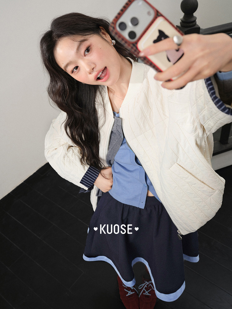 Woman wearing a cream quilted jacket and navy skirt taking a selfie