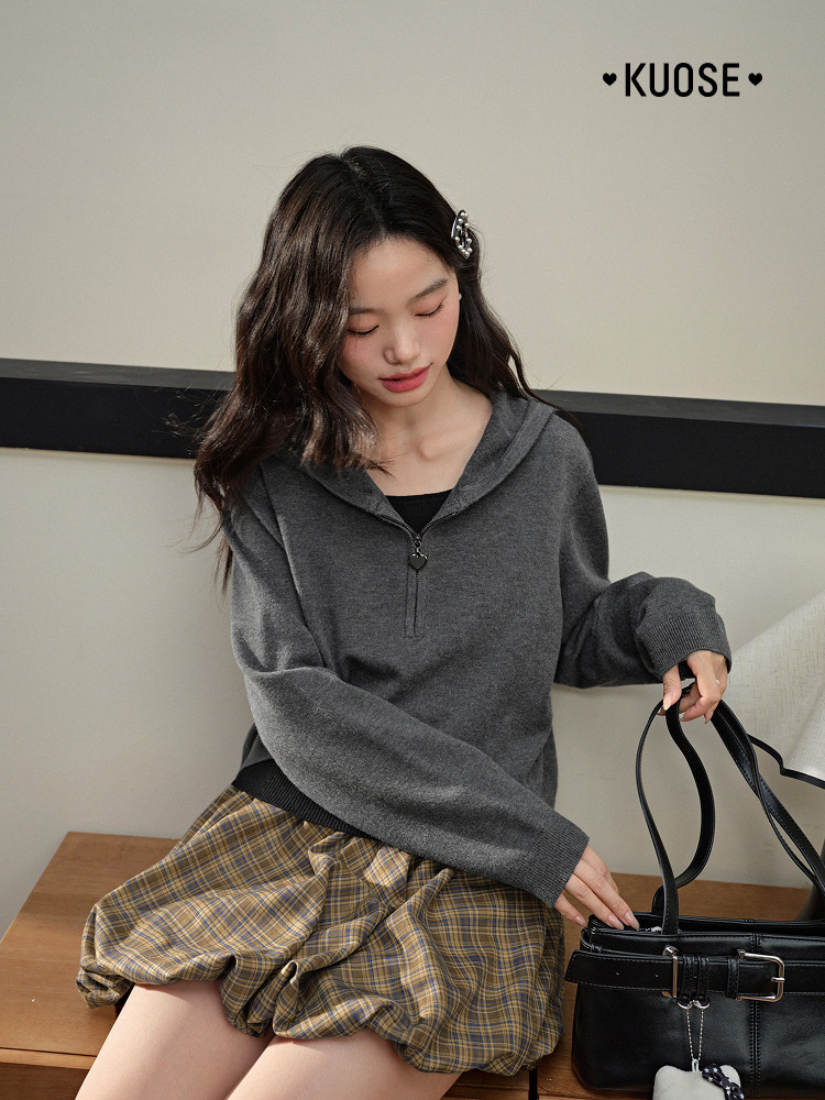 Model wearing a dark gray zip-front hoodie with a plaid skirt
