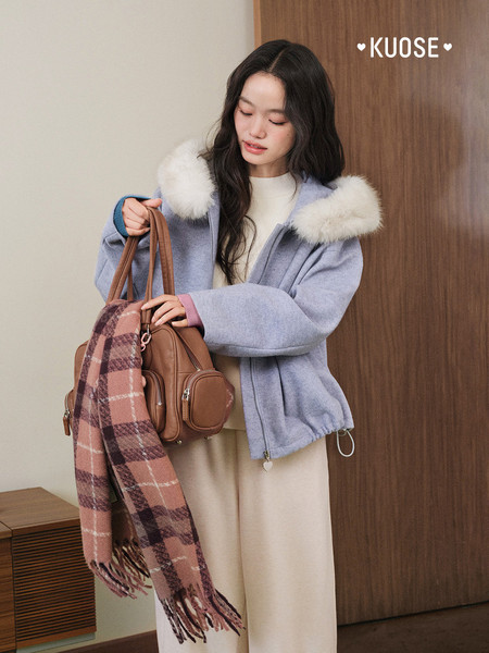 Model wearing a light blue fur-trim hooded jacket and holding a brown bag with scarf
