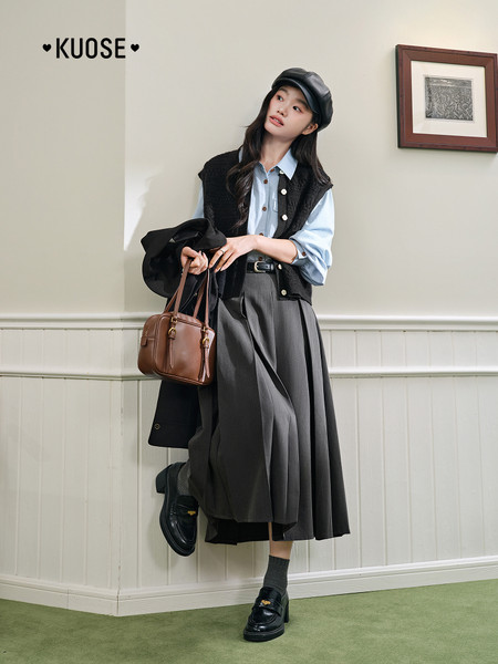 Woman wearing a preppy dark outfit with pleated skirt, shirt, vest, hat, and handbag