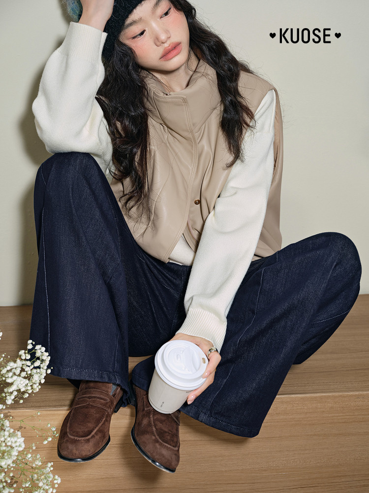 Model wearing a beige layered vest over a white sweater with dark jeans and brown shoes