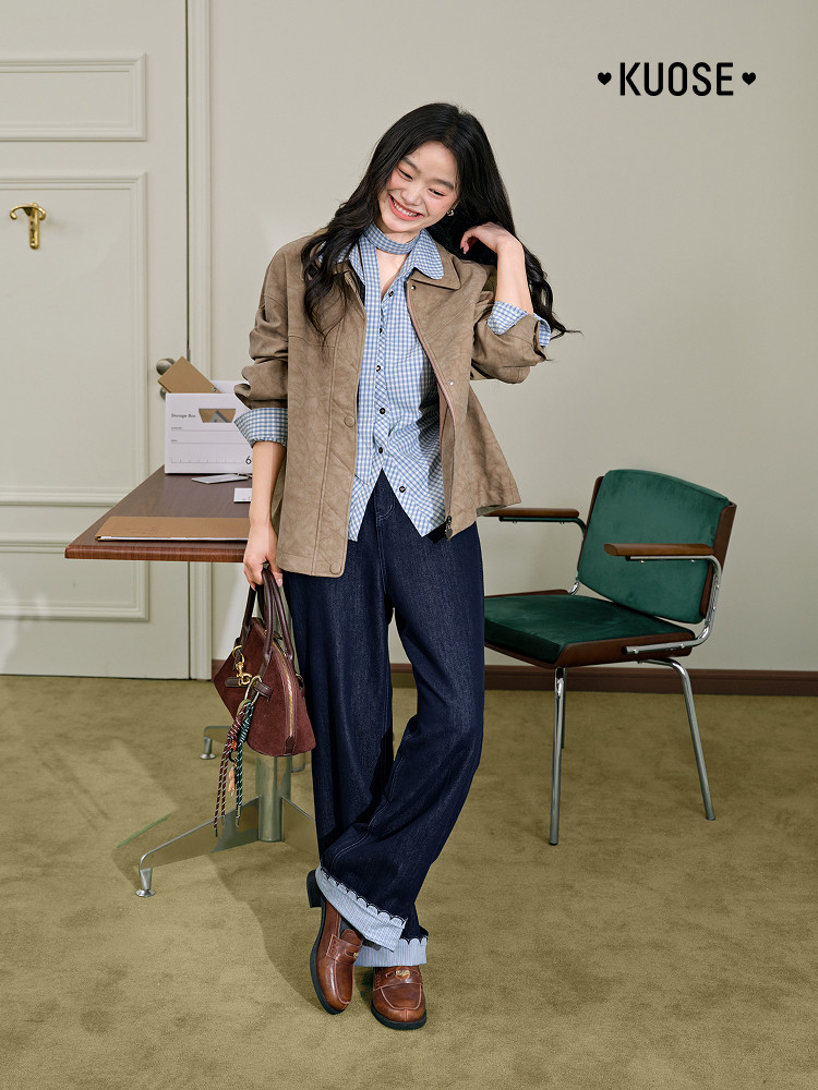 Model wearing a tan jacket over a blue gingham shirt with dark wide-leg jeans and brown loafers