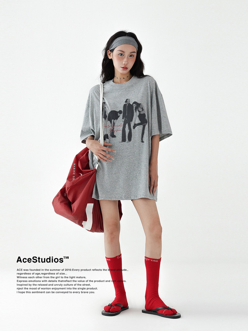 Model wearing an oversized gray graphic T-shirt dress with a red shoulder bag and red socks