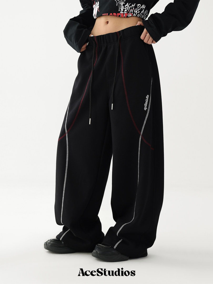 Model wearing black wide-leg streetwear pants with contrast stitching and drawstring waist