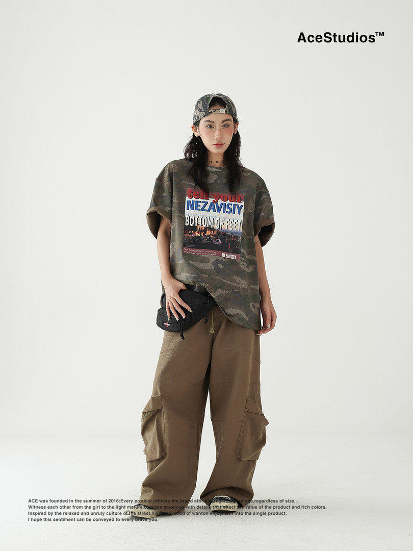 Model wearing an oversized camouflage graphic T-shirt with cargo pants and a cap