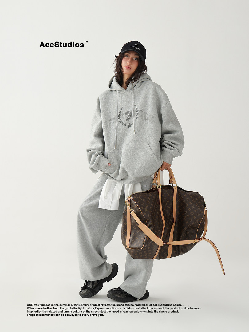 Model wearing an oversized gray hoodie and sweatpants while holding a monogram duffel bag