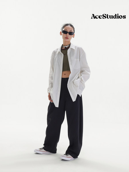 Model wearing a white striped oversized shirt with black wide-leg pants and sneakers