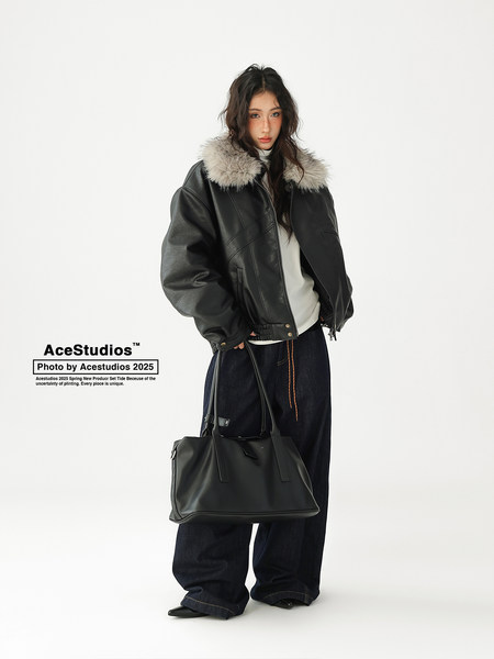 Model wearing a black leather jacket with faux fur collar and carrying a black tote bag