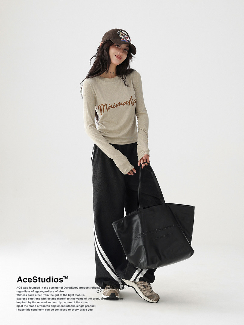Model wearing a beige long-sleeve top and black wide-leg pants with a black tote bag