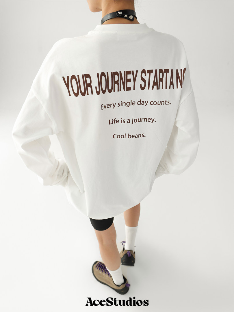 White oversized long-sleeve top worn by a model with large brown slogan text on the back