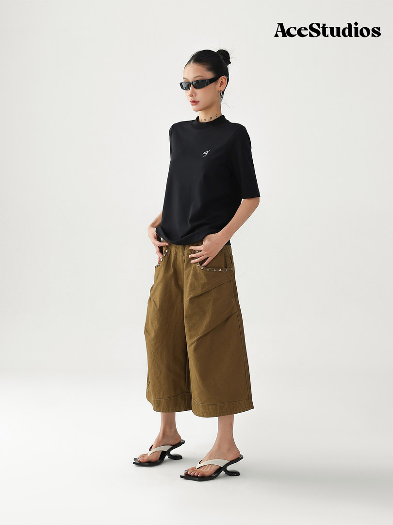 Model wearing a black short-sleeve top with wide brown cropped pants and flip-flops