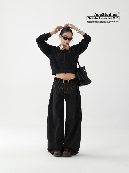 Model wearing a black cropped jacket and wide-leg jeans with sunglasses and a shoulder bag