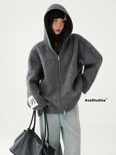 Model wearing a gray hooded zip-up fuzzy jacket with a black bag