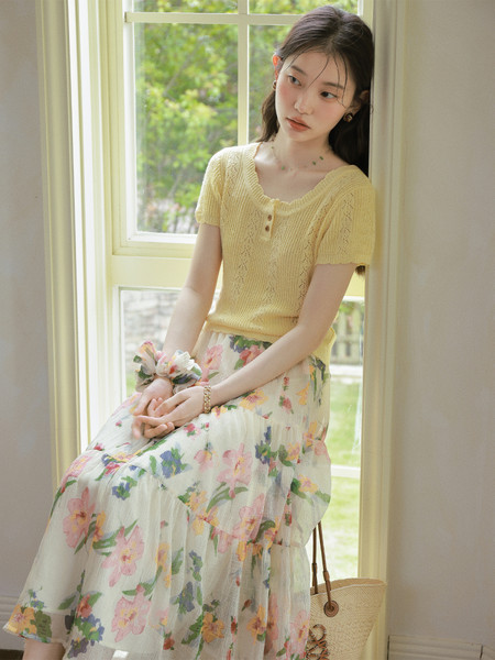 Model wearing a yellow knit short-sleeve top with a floral skirt by a window