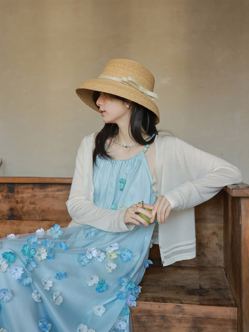 Woman wearing a light blue floral dress with a white cardigan and straw hat