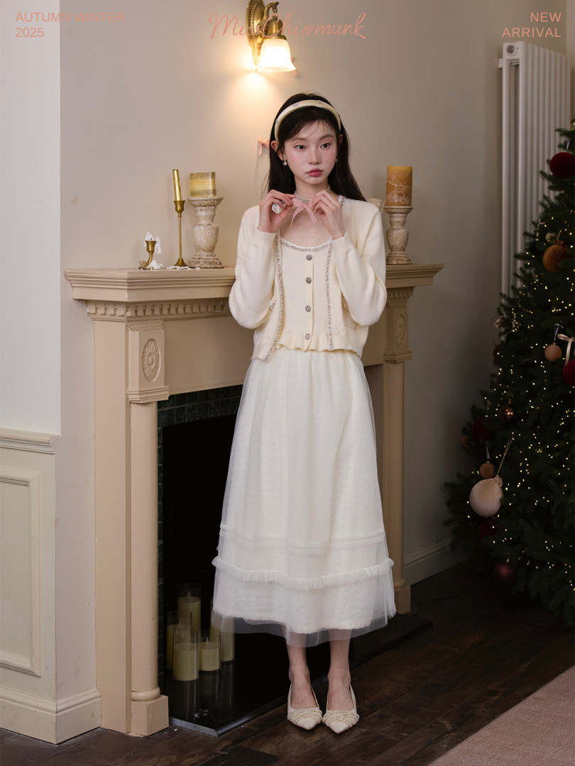 Model wearing a cream cardigan and long white dress in an indoor holiday setting