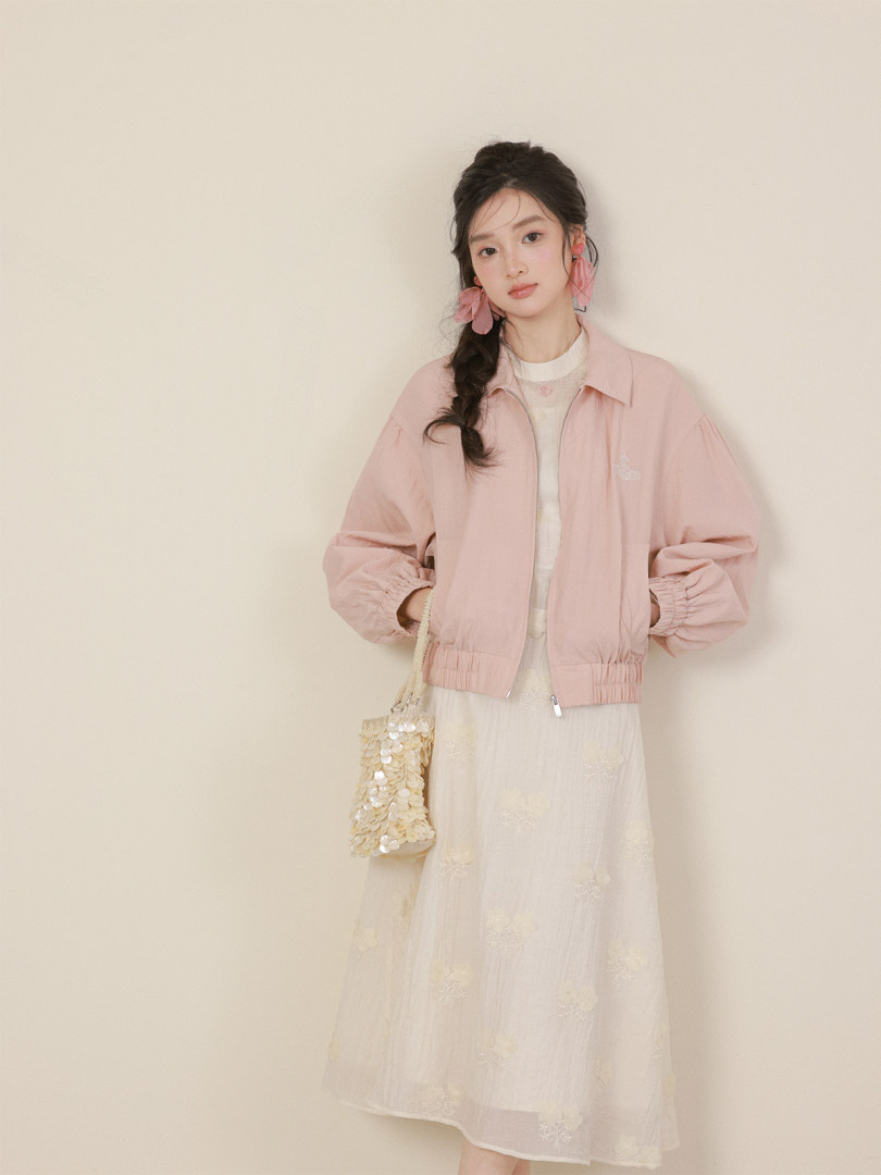 Model wearing a light pink jacket over a cream dress with a small beaded handbag