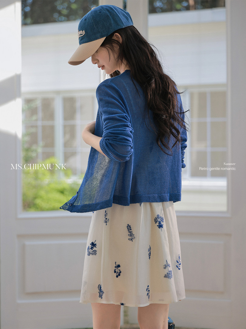 Woman wearing a blue cardigan over a floral dress with a baseball cap