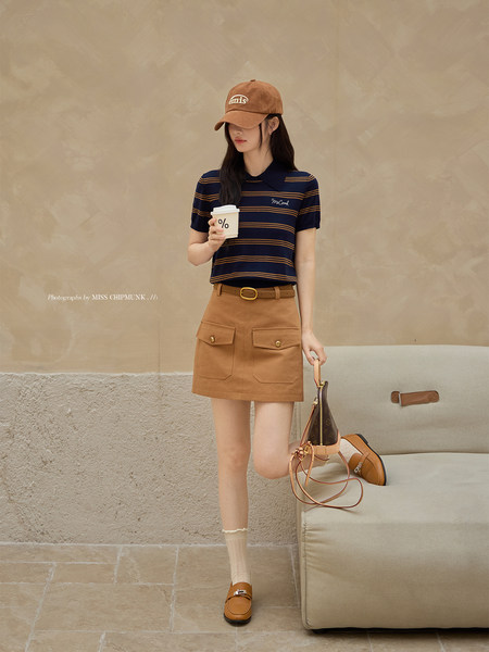 Model wearing a navy striped polo top with a brown mini skirt, cap, loafers, and a handbag
