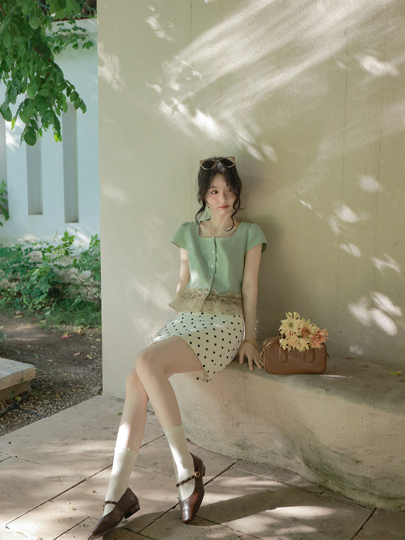 Model wearing a light green top and polka dot skirt with a brown handbag outdoors