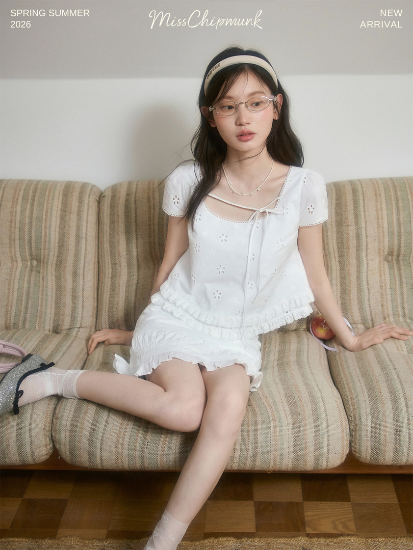 Young woman wearing a white ruffled dress and glasses on a couch
