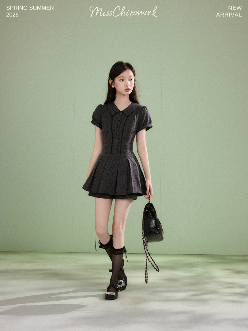 Model wearing a black short-sleeve pleated dress with a handbag