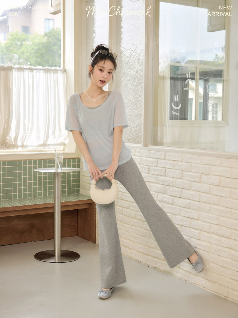 Model wearing a light gray casual top and wide-leg pants with a small handbag