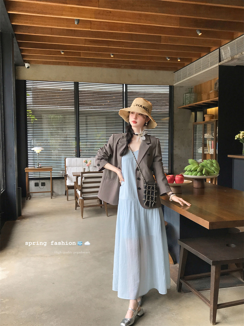 Woman wearing a light blue dress with a brown blazer, hat, and crossbody bag indoors