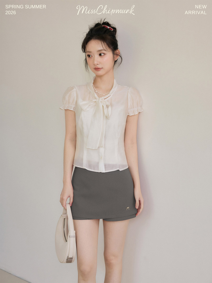 Model wearing a white bow-tie blouse with a gray mini skirt and handbag